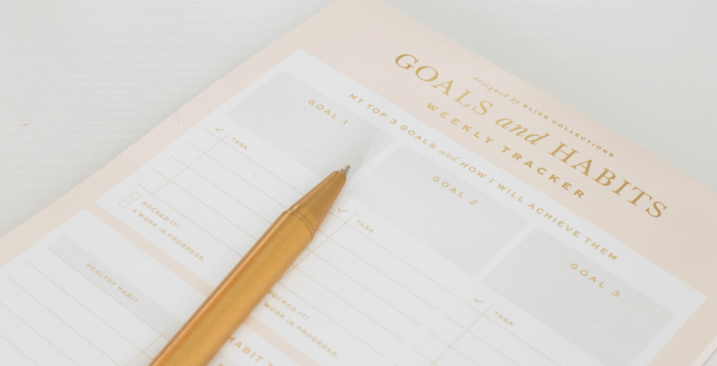 Goal and habit tracker with a pen on a desk, representing intention setting, new year goals, and the difference between intentions vs goals and resolutions vs goals.