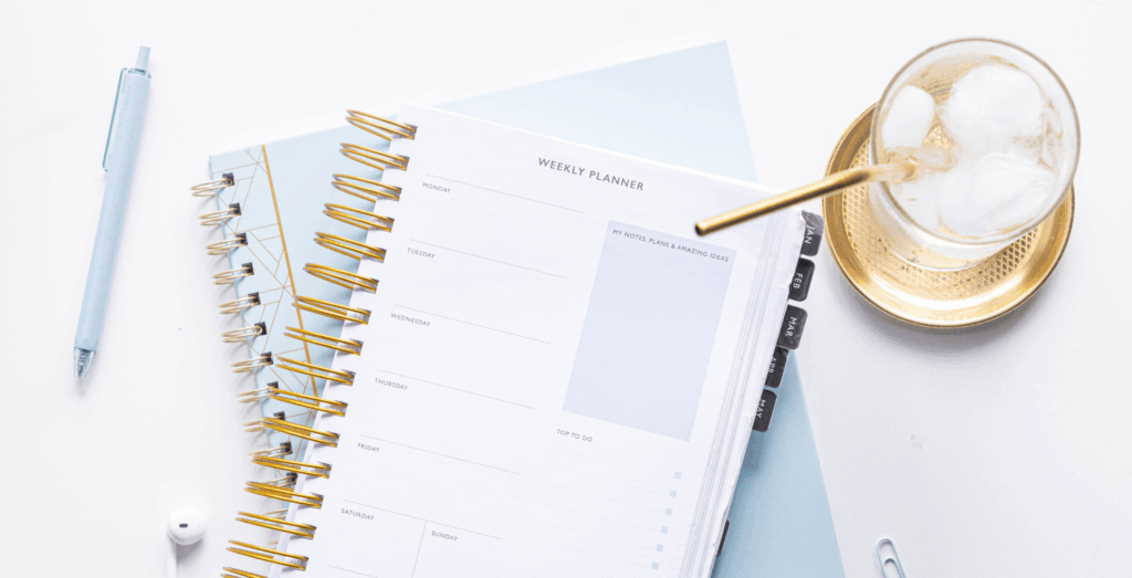 Weekly planner open on a desk with a pen and iced drink, symbolizing setting goals, sustainable goal setting, and a focused goal setting mindset for how to achieve goals.