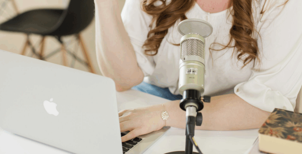 Entrepreneur working at laptop with microphone, representing solopreneur tips for business success, showing how to stay consistent and follow through without all or nothing thinking.