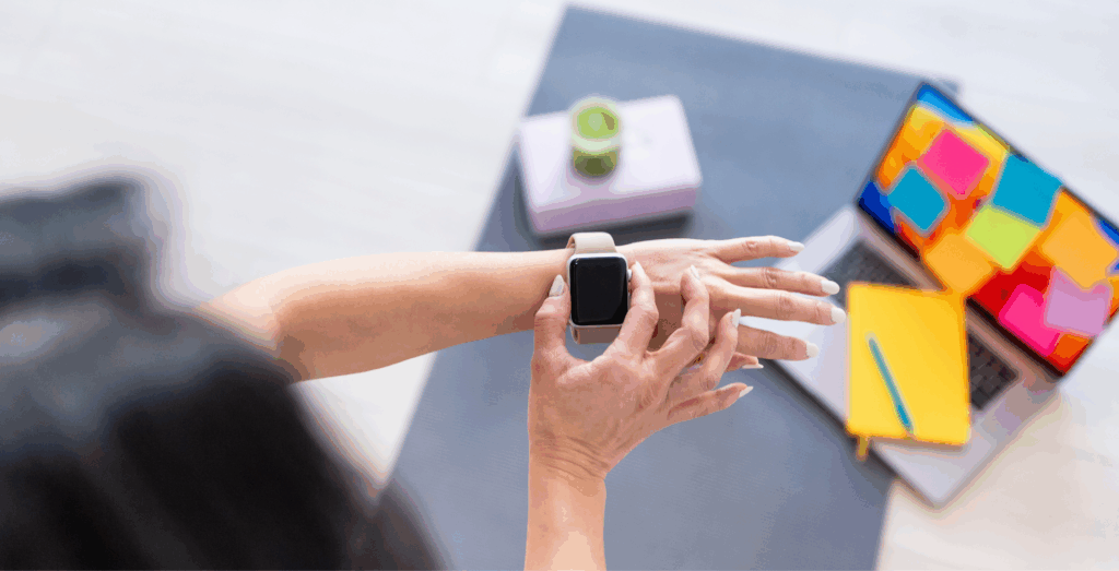Entrepreneur checking smartwatch at desk with laptop and notes, representing how to stay consistent, improve productivity, and follow through with daily actions instead of all or nothing thinking.