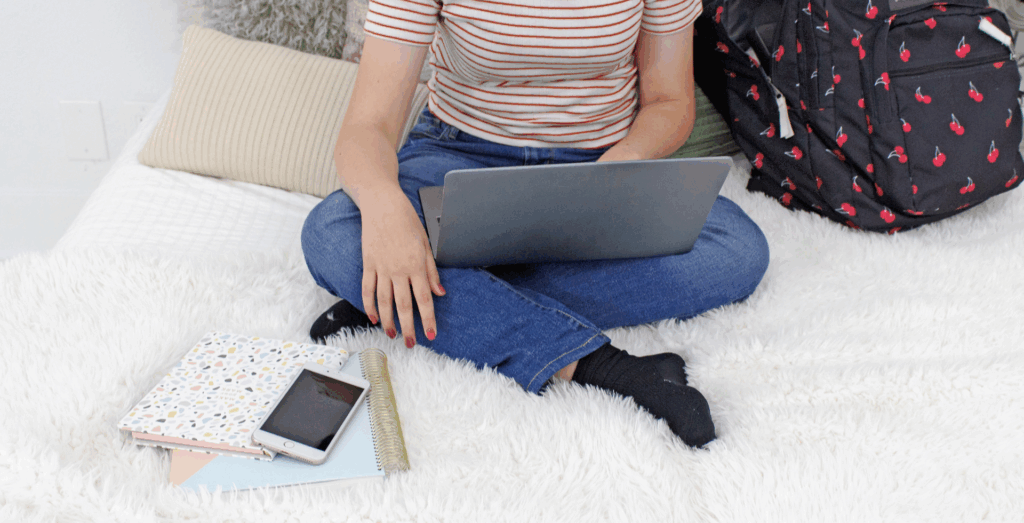 Person using a laptop in a casual workspace surrounded by notebooks and tech devices, showing entrepreneurs waiting to build systems because they feel overwhelmed by choosing tools and trying to stop waiting to get organized.