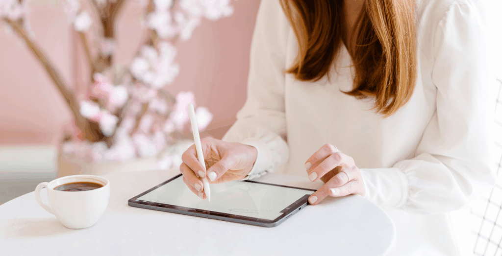 Small business owner using a tablet at a clean workspace with coffee nearby, demonstrating small business systems, digital organization, and building systems that simplify workflows and strengthen business systems.
