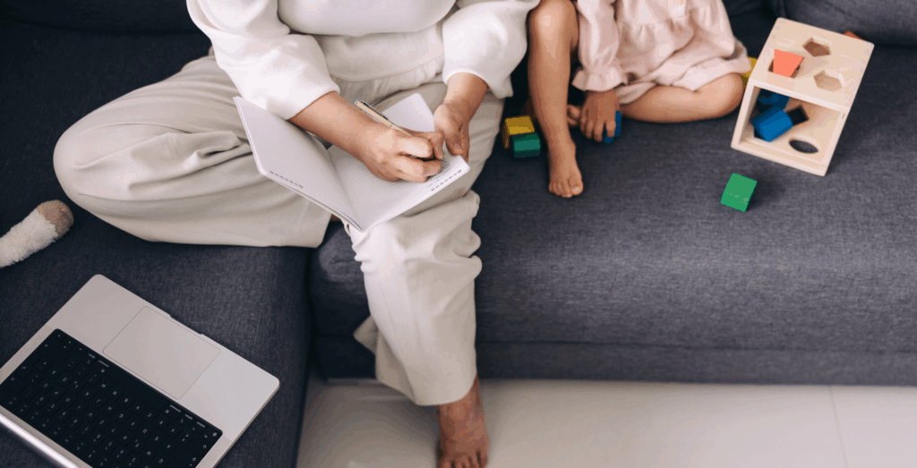 Solopreneur parent managing notes and childcare at home, representing the mental load and invisible workload many entrepreneurs carry while balancing routines, habits, boundaries, and home systems for solopreneurs to avoid constantly feeling overwhelmed.