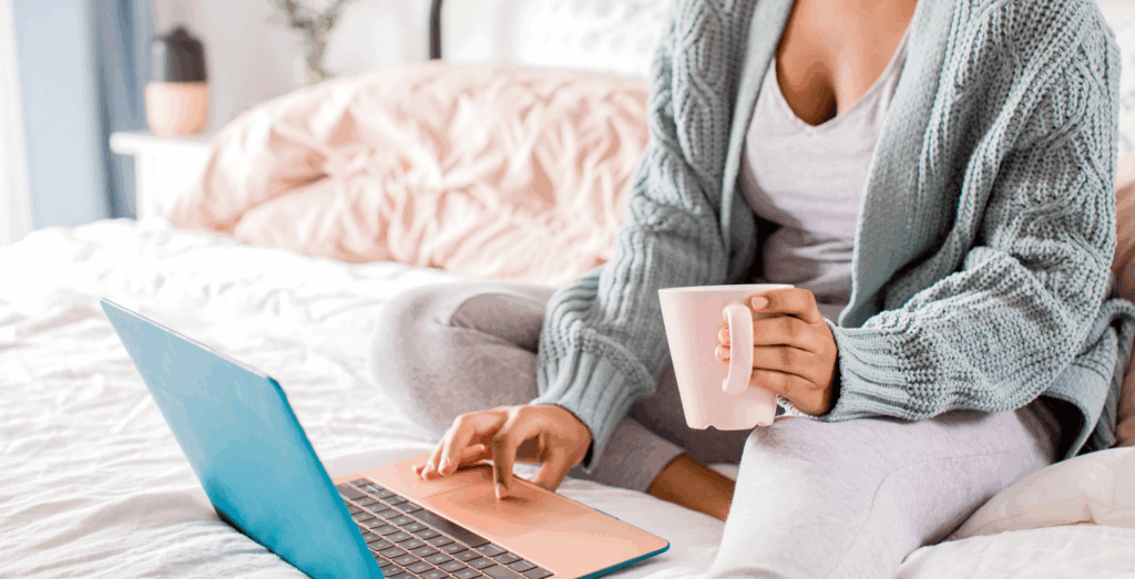 Overwhelmed solopreneur sitting on a bed with coffee and a laptop, illustrating feeling overwhelmed while trying to balance work and life with simple systems and sustainable routines.