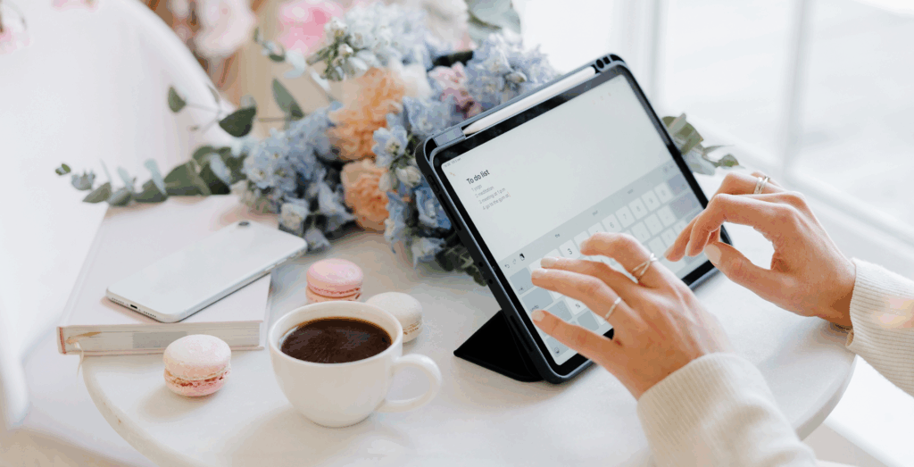 Solopreneur organizing a digital to-do list on a tablet beside coffee and notebooks, highlighting life systems, supportive routines, and practical habits that reduce mental load, strengthen boundaries, and prevent the invisible workload that leaves entrepreneurs feeling overwhelmed.